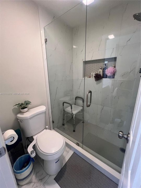 Walk-in shower featuring glass enclosure, floor-to-ceiling large-format tile, recessed wall niche, and an overhead shower head