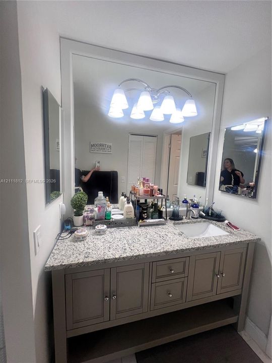 Bathroom vanity featuring neutral-toned cabinetry, a stone-composite countertop, an integrated rectangular undermount sink, and a large wall-to-wall mirror with a six-light fixture