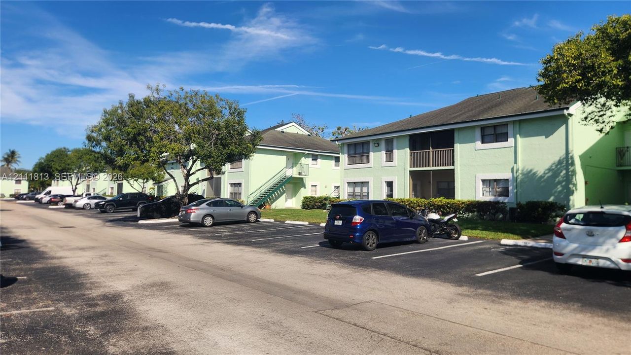Multi-story exterior featuring light-colored stucco siding, a pitched roof, screened balconies, and dedicated surface parking