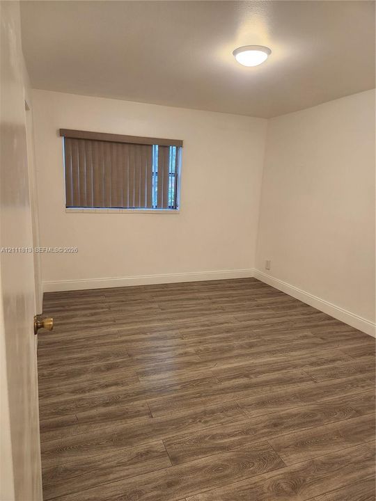 Room interior featuring wood-finish flooring, white walls, and a ceiling-mounted light fixture