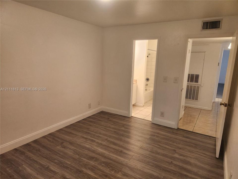 Room interior featuring wood-finish flooring, neutral wall tones, and ceramic tile flooring in the entry area