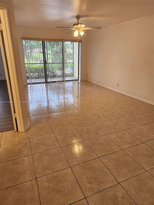 Living space featuring oversized square tile flooring, ceiling-mounted fan with integrated lighting, and glass sliding doors