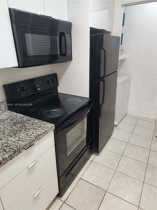 Kitchen featuring white flat-panel cabinetry, stone-patterned countertops, black appliances, and ceramic tile flooring