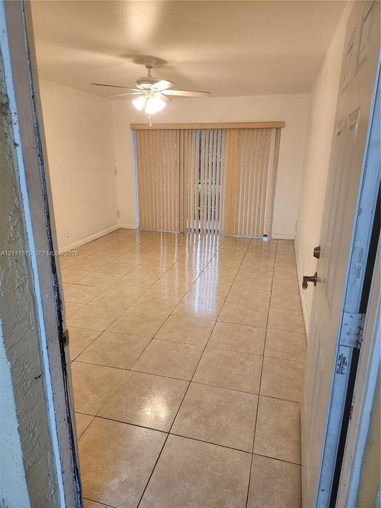 Interior space featuring large-format ceramic tile flooring, a multi-blade ceiling fan with integrated light fixture, and floor-to-ceiling vertical blinds