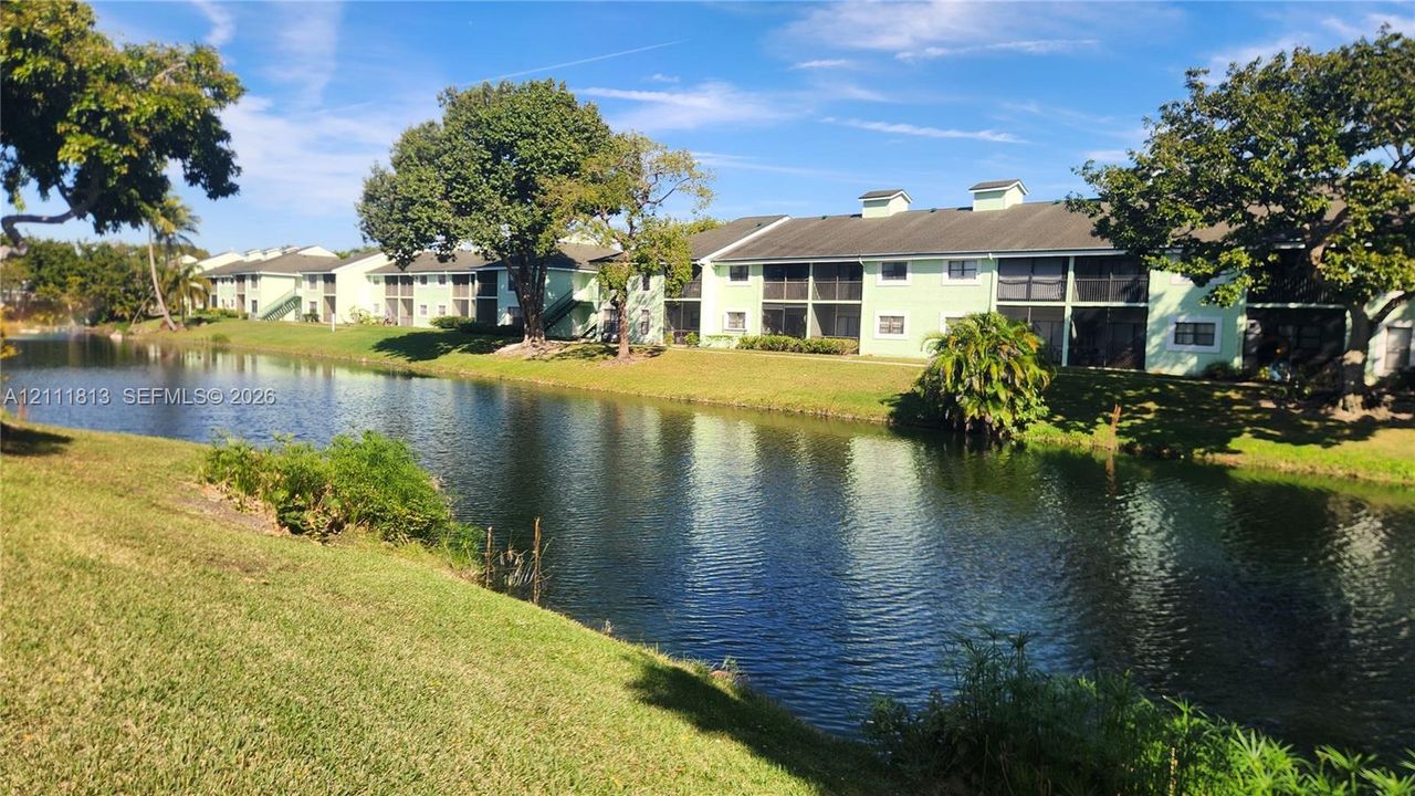 Waterfront multi-unit building featuring screened-in lanais, manicured landscaping, and mature shade trees