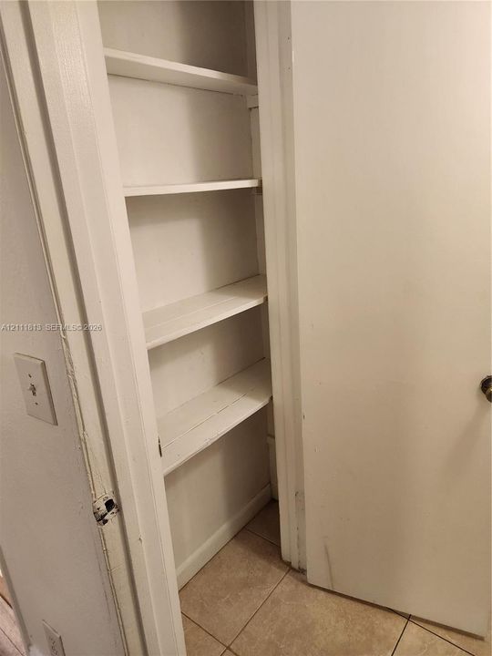 Built-in storage closet featuring painted white shelving and tile flooring