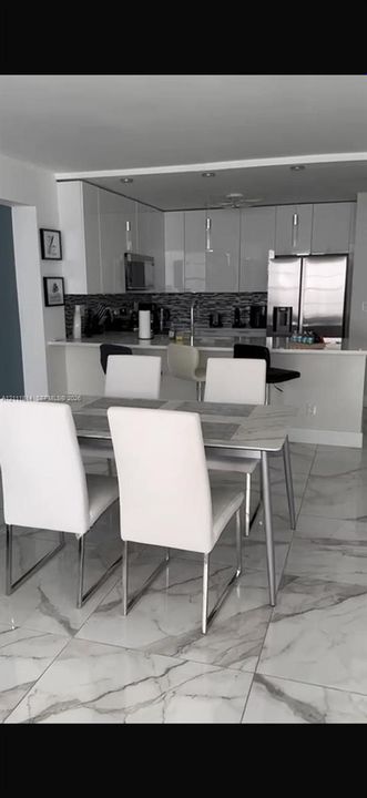 Kitchen featuring flat-panel high-gloss cabinetry, stone-finish countertops, stainless steel appliances, mosaic tile backsplash, and large-format tile flooring