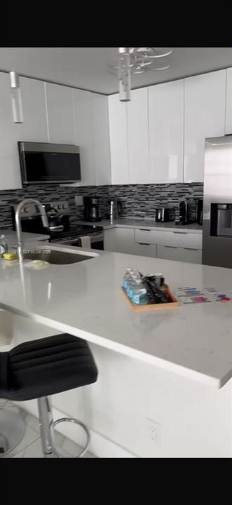 Kitchen featuring gloss-finish cabinetry, stone-surface countertops, stainless steel appliances, a multi-tone tile backsplash, and a built-in island