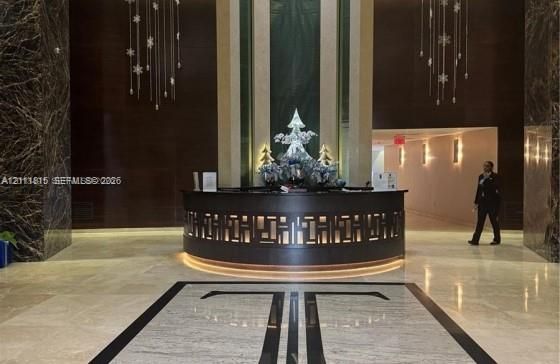 Grand lobby featuring stone flooring with inlaid detailing, dark stone accent walls, a curved reception desk with integrated lighting, and tiered crystal light fixtures