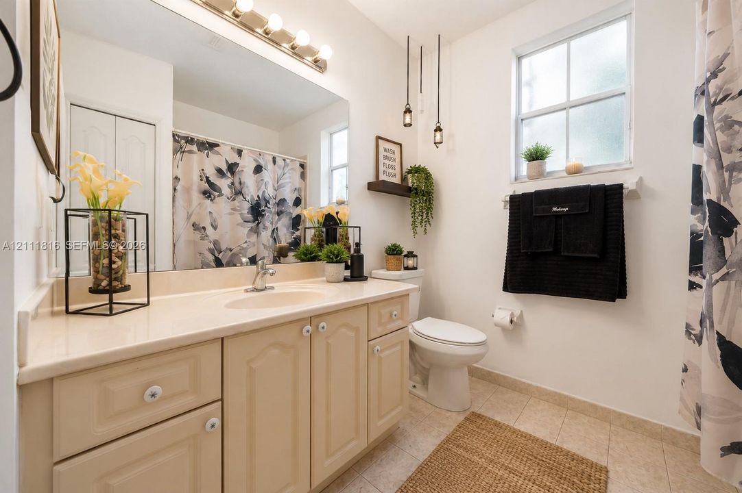 Bathroom featuring a vanity with integrated sink and countertop, large wall-mounted mirror, multi-light vanity fixture, pendant lighting, and ceramic tile flooring