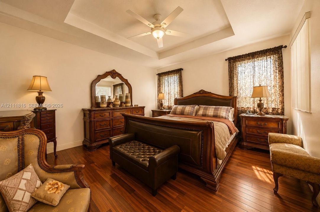 Tray ceiling featuring a central white ceiling fan with integrated lighting and wood-finish flooring
