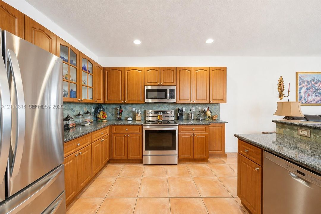 Kitchen featuring stained wood cabinetry, stone countertops, stainless steel appliances, a decorative tile backsplash, and tile flooring