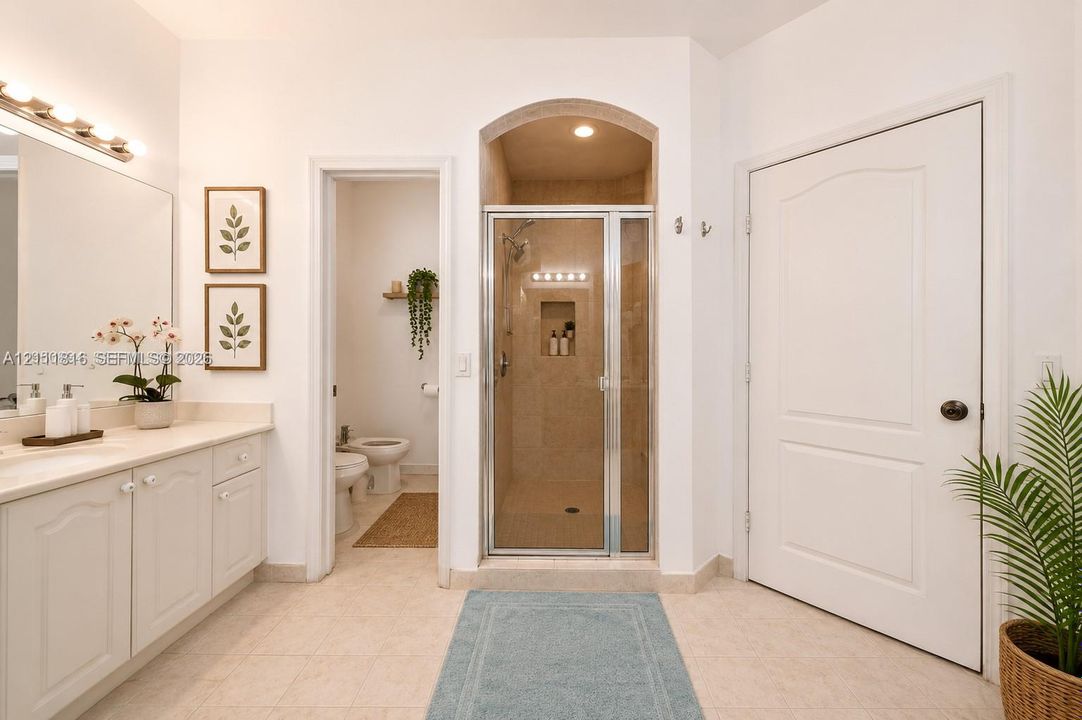 Bathroom featuring a neutral-toned vanity with an integrated countertop, a walk-in shower enclosure set within an arched alcove, a separate water closet area, and tile flooring