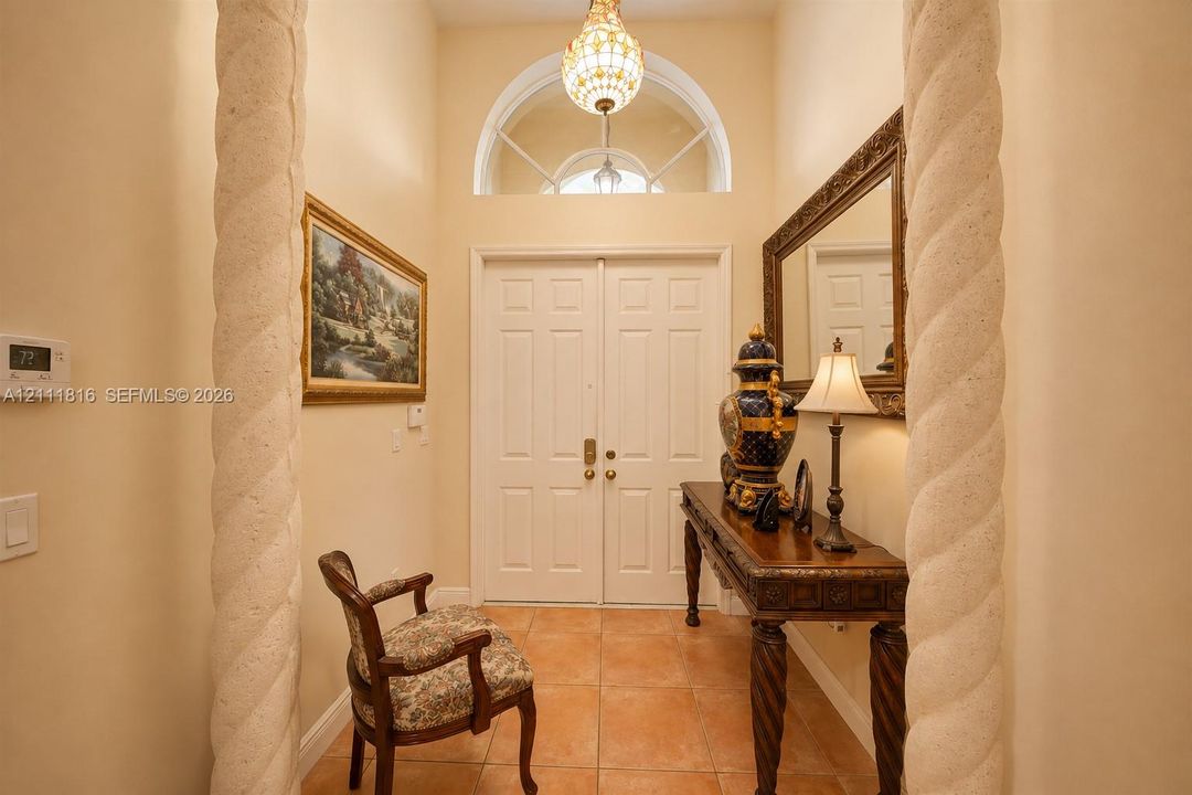 Entryway featuring double doors, stone-finish spiral columns, ceramic tile flooring, and a decorative arched transom window with a tiered glass chandelier