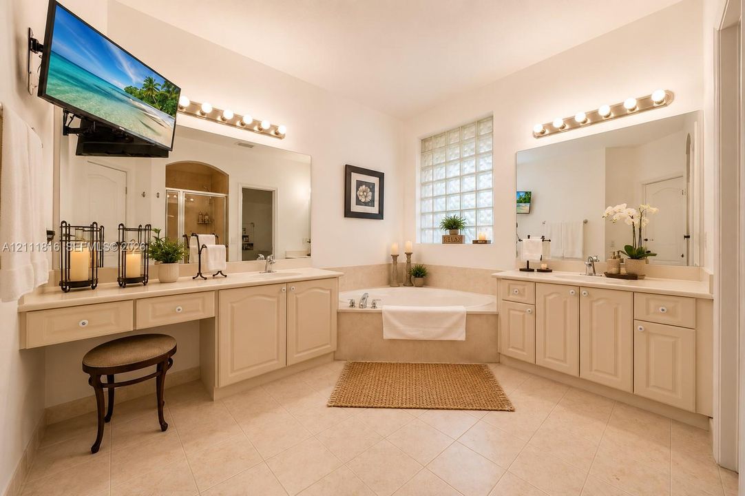 Dual vanities with solid-surface countertops, built-in cabinetry, soaking tub, glass block window, and dual wall-mounted vanity lighting