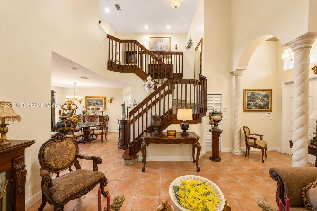 Foyer featuring a multi-story ceiling, decorative columns, tile flooring, and an open staircase with wood railings