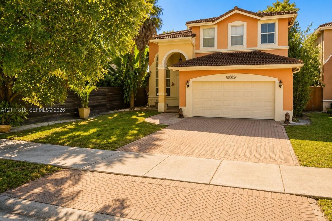 Two-story exterior featuring a stucco façade, tiled roof, arched entryway, and a herringbone-patterned paved driveway