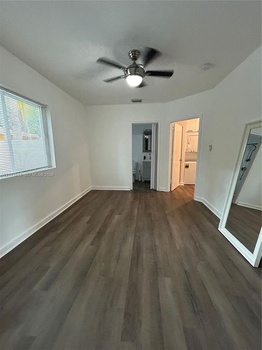Room featuring wood-finish flooring, a ceiling fan with integrated lighting, and a window with blinds