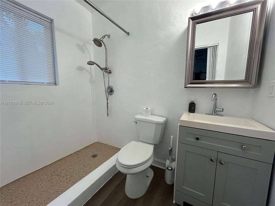 Bathroom featuring a grey-finish vanity with an integrated basin, a walk-in shower with a dual-head fixture, wood-finish flooring, and a framed wall-mounted mirror