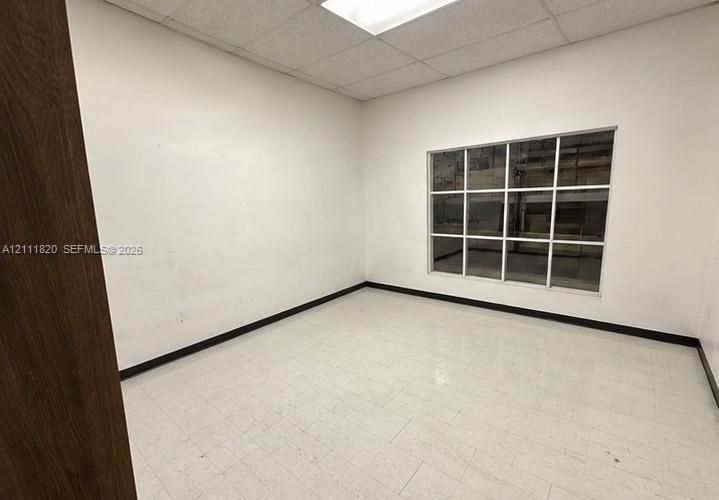 Interior room featuring white walls, white tile flooring, drop ceiling, and a large multi-pane interior window
