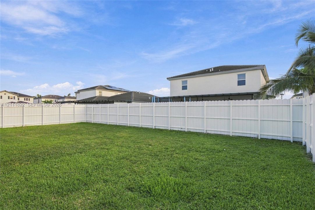 Expansive backyard featuring a level lawn and white vinyl privacy fencing