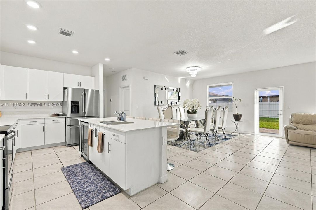 Kitchen featuring white cabinetry, an island with a stone-finish countertop and integrated sink, stainless steel appliances, recessed lighting, and tile flooring