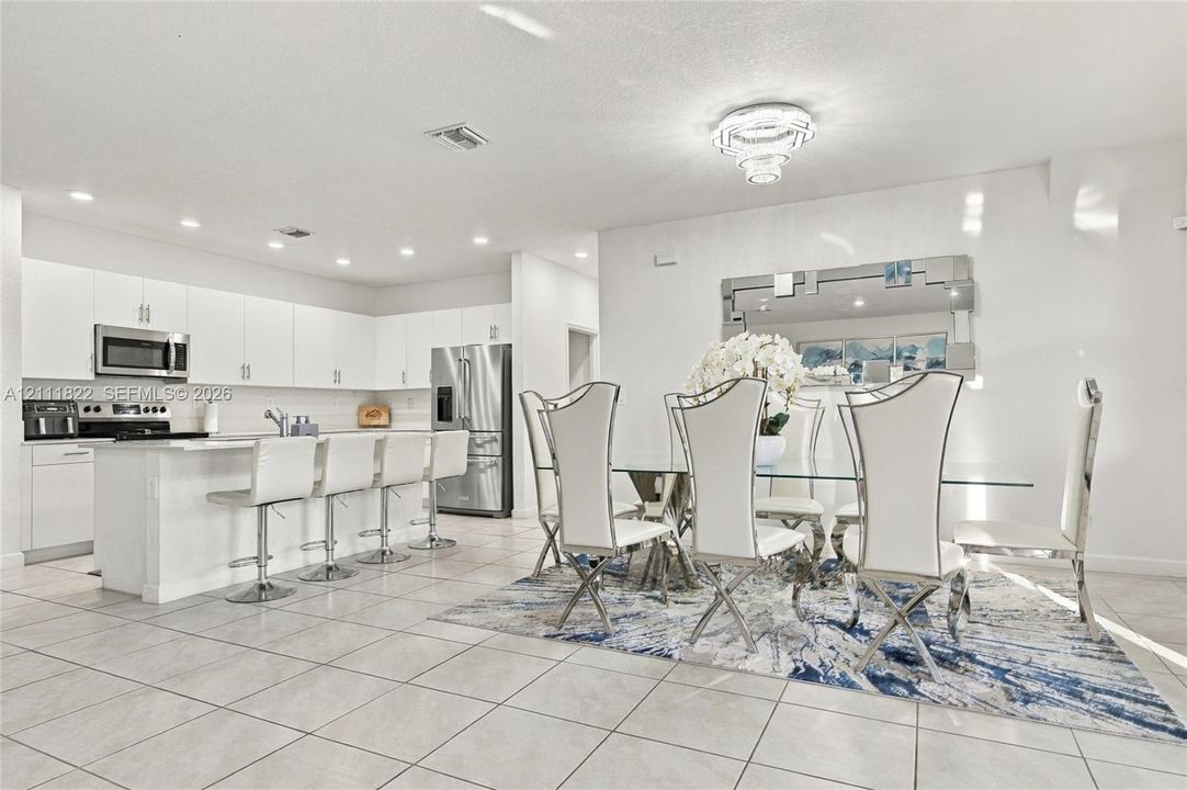Kitchen featuring white shaker cabinetry, stainless steel appliances, a center island with bar seating, recessed lighting, and tile flooring