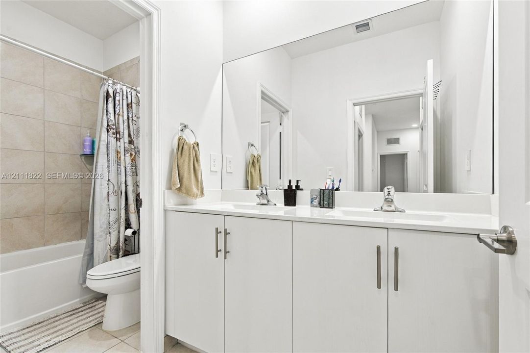 Bathroom featuring a dual-sink vanity with a solid-surface countertop, floor-to-ceiling mirror, and a tile-surround bathtub