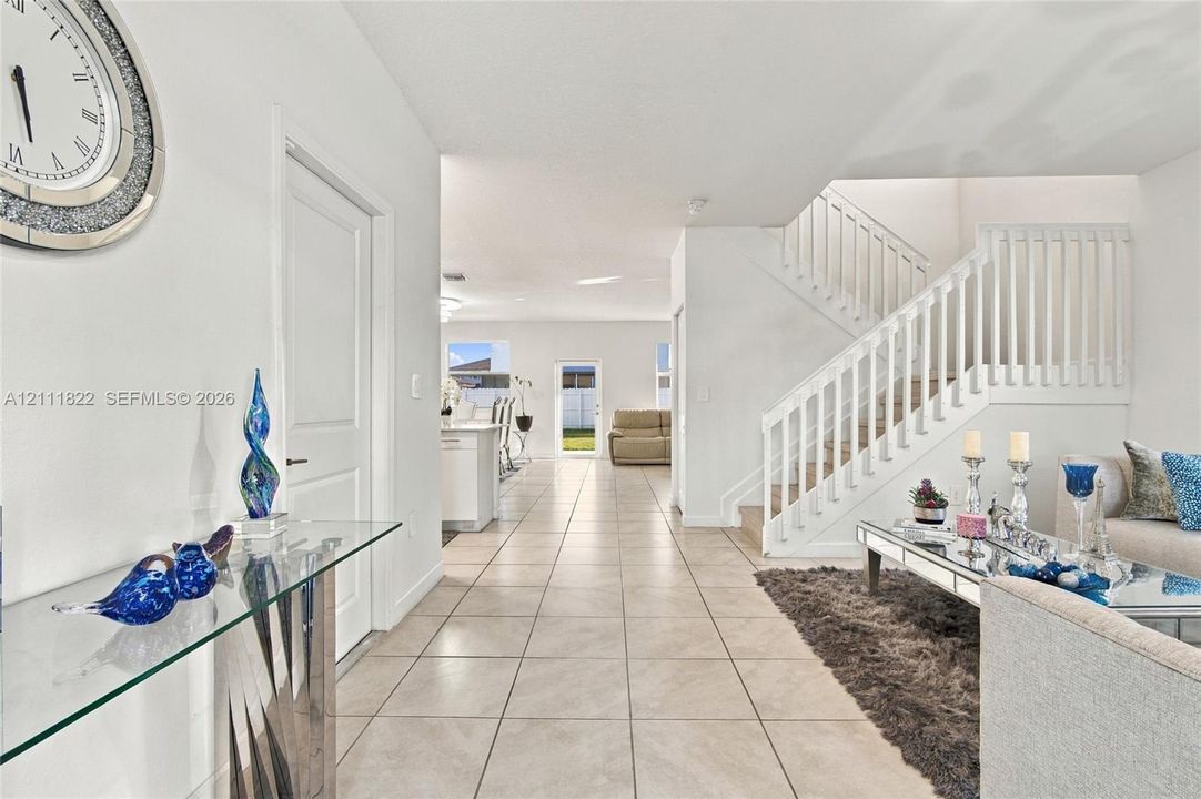 Open floor plan featuring neutral tile flooring, a white staircase with a vertical balustrade, and a glass-paned exterior door