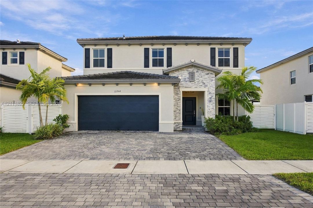 Two-story residence featuring a stone-veneer entryway, paver driveway, dark-toned garage door, and decorative exterior shutters