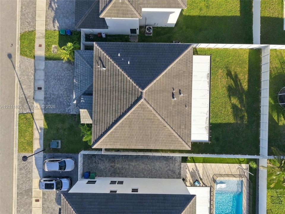 Aerial perspective featuring a tile roof, paved driveway, enclosed backyard, and swimming pool