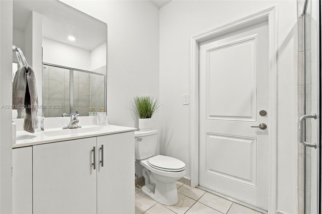Bathroom featuring a vanity with a white countertop and integrated sink, a large wall-mounted mirror, a two-panel interior door, and a tiled shower enclosure
