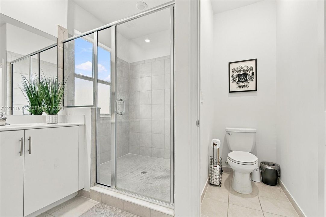 Walk-in shower with chrome-framed glass enclosure, tiled surround, white vanity cabinet, rectangular under-mount sink, and ceramic tile flooring