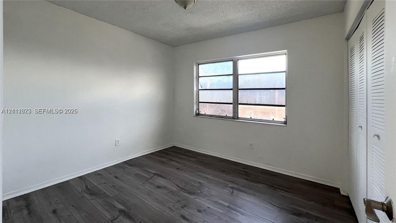 Room featuring wood-finish flooring, white walls, horizontal window, and dual bi-fold louvered closet doors