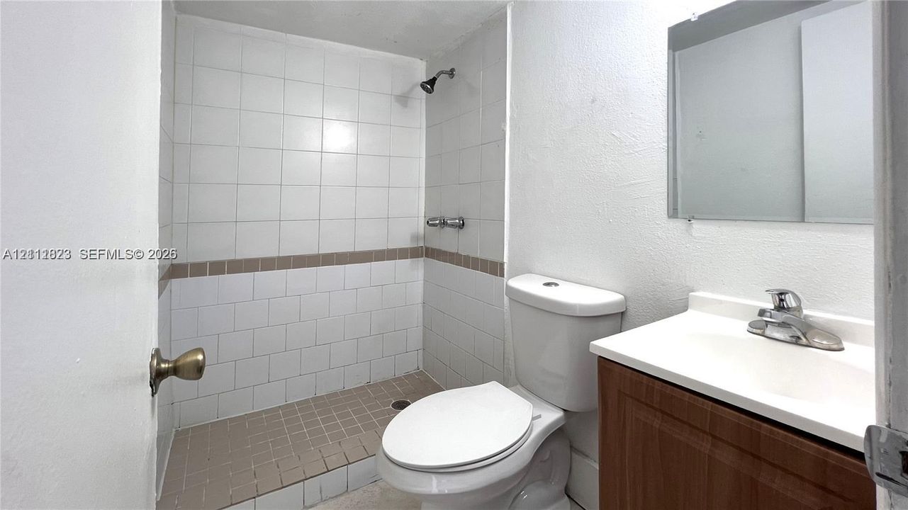 Bathroom featuring a wood-finish vanity, integrated sink, wall-mounted mirror, and walk-in shower with tiled surround