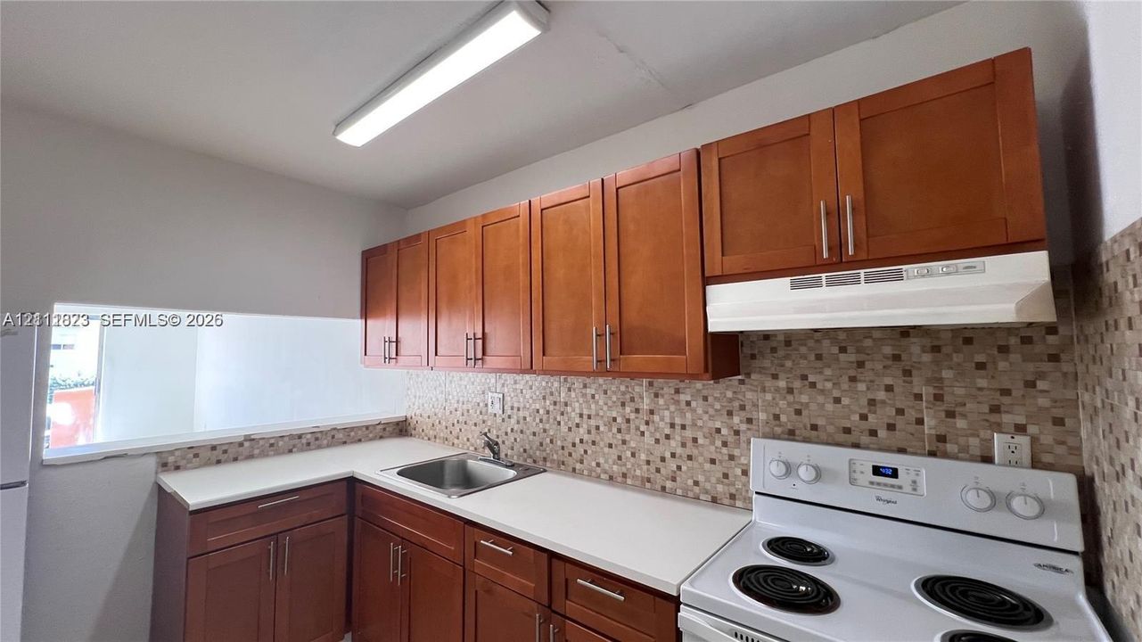 Kitchen featuring wood cabinetry, solid-surface countertops, mosaic tile backsplash, stainless steel sink, and white electric range