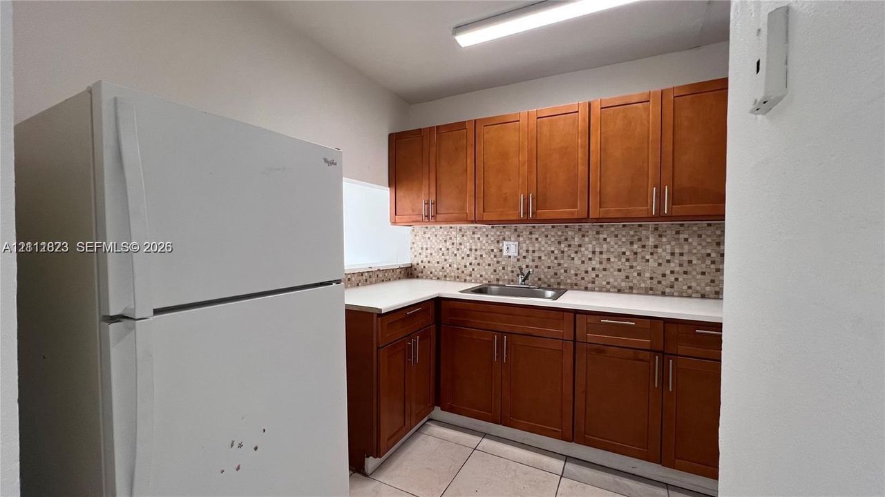 Kitchen area featuring wood cabinetry, white countertops, a mosaic tile backsplash, a stainless steel sink, and a white refrigerator