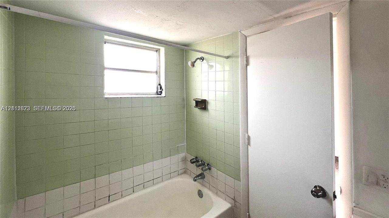 Bathroom featuring a standard white bathtub with chrome plumbing fixtures, wall-mounted shower head, integrated soap dish, and two-tone ceramic tile surround