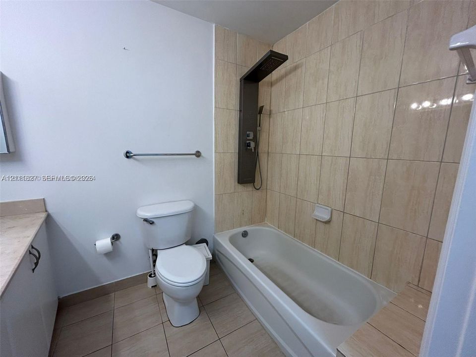 Bathroom featuring full-height neutral ceramic wall tile, soaking tub, wall-mounted multi-function shower panel, and light-toned floor tile