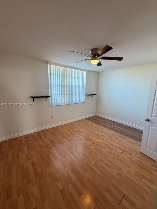 Room featuring wood-finish flooring, a ceiling fan with integrated lighting, wall-mounted shelving, and window blinds