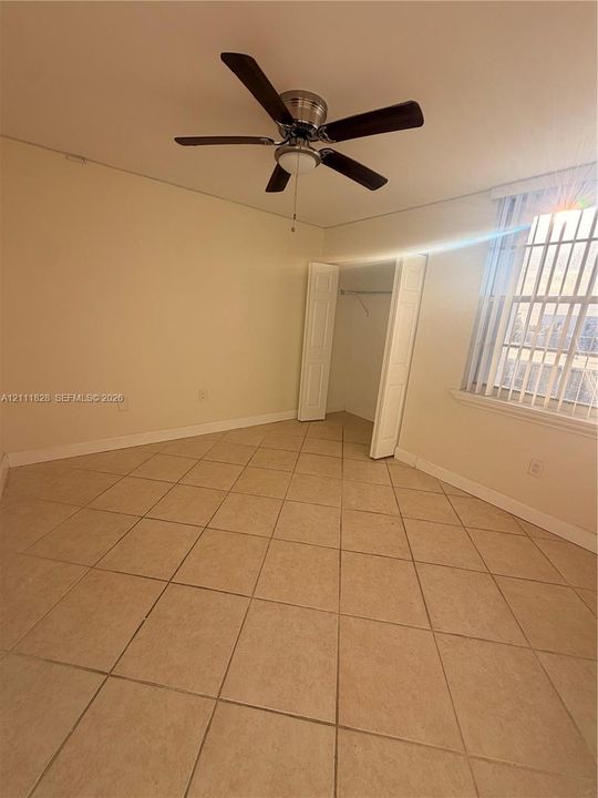 Room featuring neutral ceramic tile flooring, a multi-blade ceiling fan with integrated light fixture, a closet with bi-fold doors, and a window with horizontal blinds