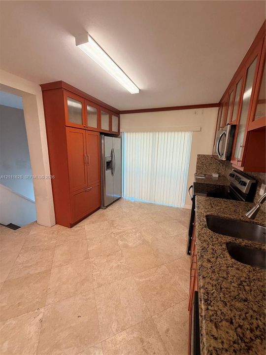 Kitchen featuring custom cabinetry with glass-panel upper doors, stone-finish countertops, tile flooring, and integrated stainless steel appliances