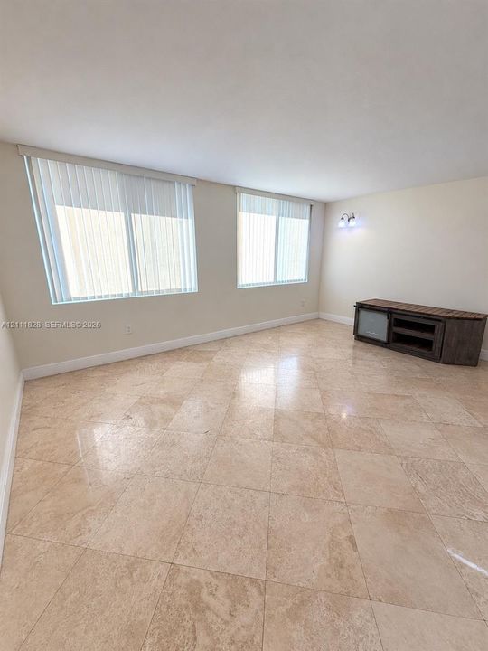 Neutral-toned stone flooring arranged in a diagonal pattern, dual windows featuring vertical blinds, and wall-mounted accent lighting