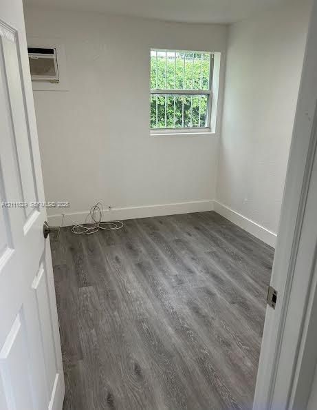 Neutral-toned wood-finish flooring, white walls, and a window featuring external security bars