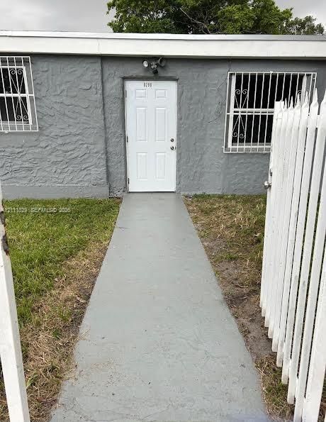 Stucco exterior facade featuring a concrete walkway, white picket fencing, and security bars on windows