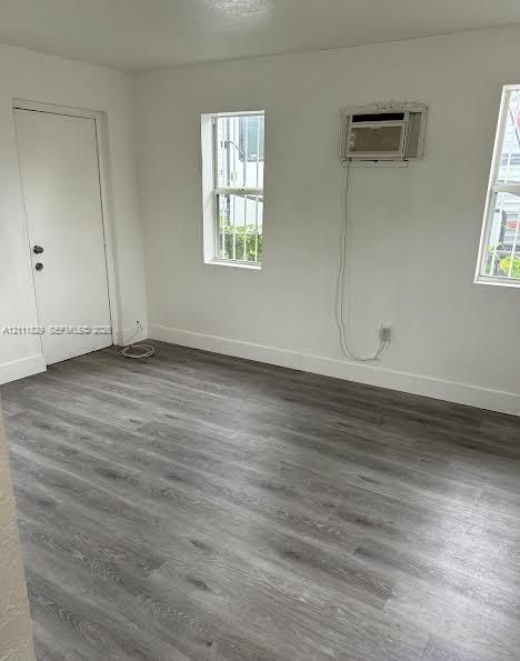 Interior room featuring wood-finish flooring, white walls, double-pane windows, and a built-in wall air conditioning unit