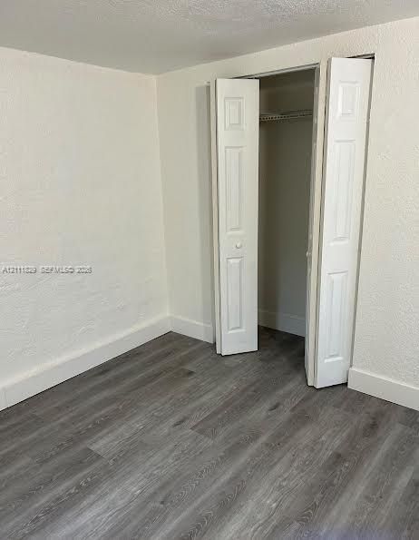 Interior space featuring wood-finish flooring, textured walls, and a closet with bifold doors and integrated shelving