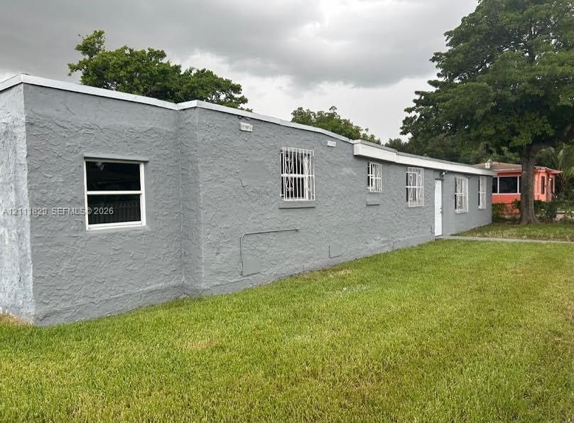 Single-story exterior featuring a textured stucco finish, flat roofline, multiple windows with security bars, and a level lawn