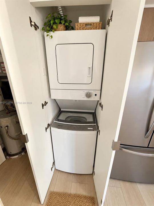 Stacked laundry unit housed within a dedicated closet featuring white cabinetry and light-toned flooring