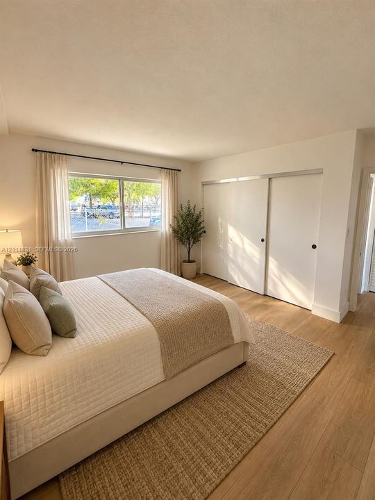 Neutral interior space featuring wood-finish flooring, a large horizontal window with a black metal rod, and built-in sliding closet doors